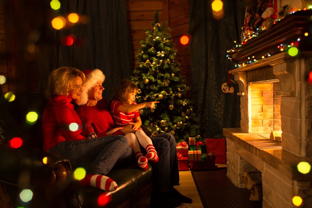 Happy family sitting by fireplace at Christmas tree.  Child shows on fire.